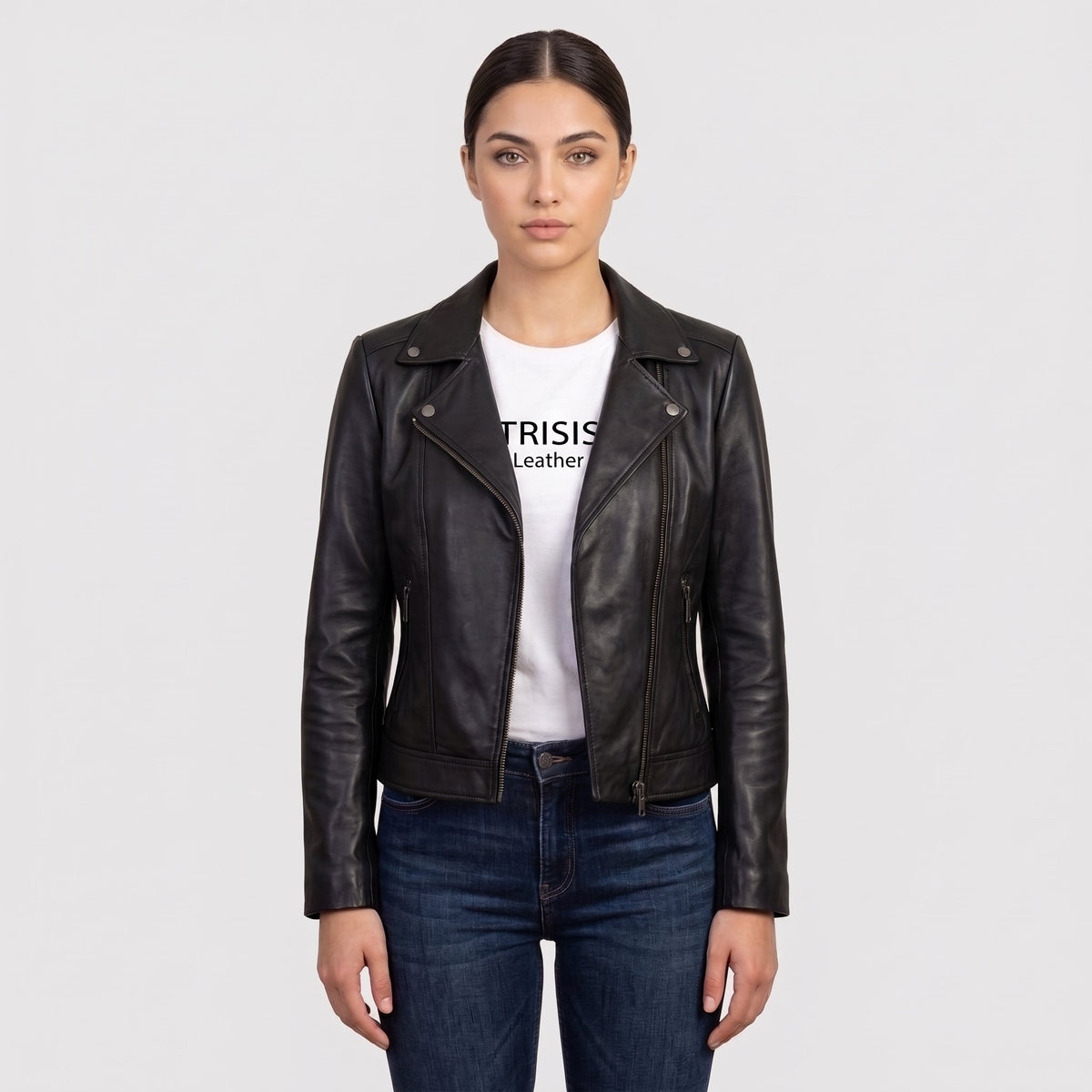 A woman modeling a black leather moto jacket over a white graphic t-shirt and dark blue jeans, shot against a solid light gray background.